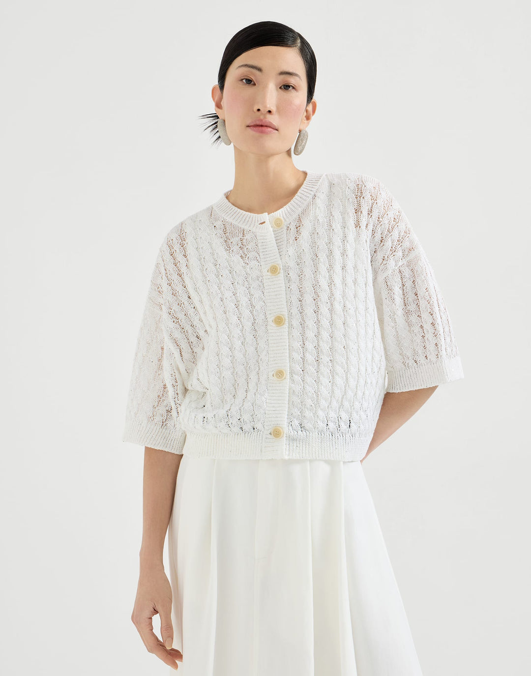 Woman wearing a white textured top with buttons on a plain background