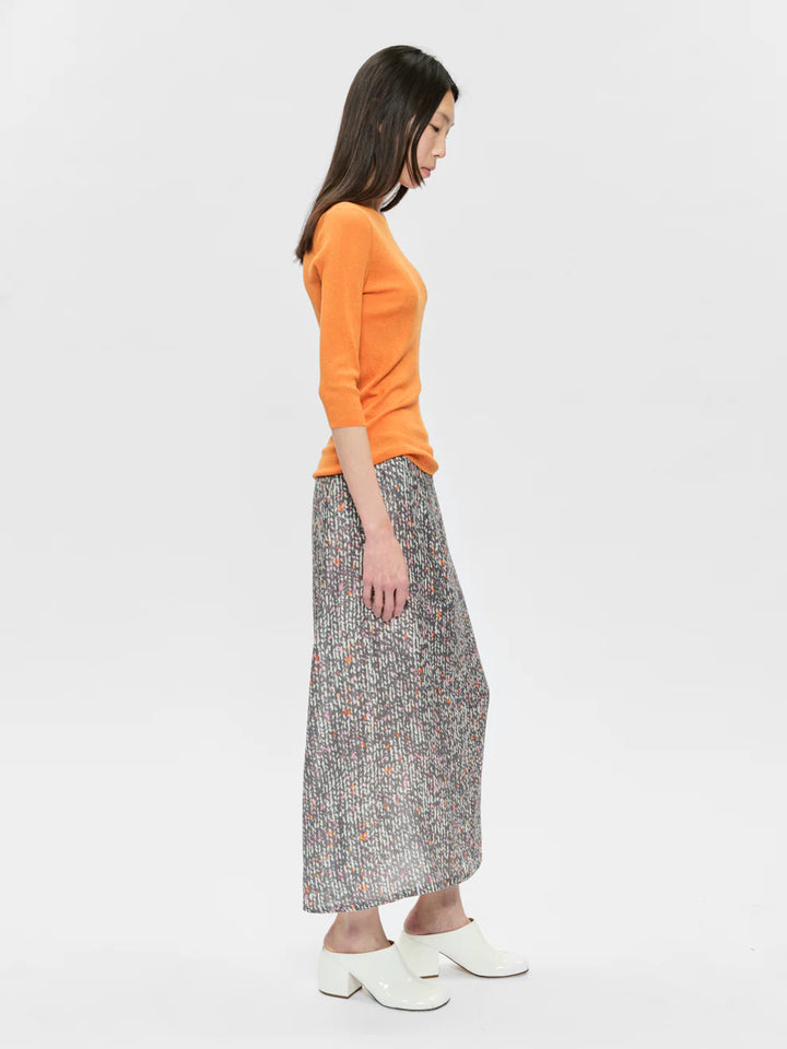 Woman wearing an orange sweater and patterned skirt on a white background