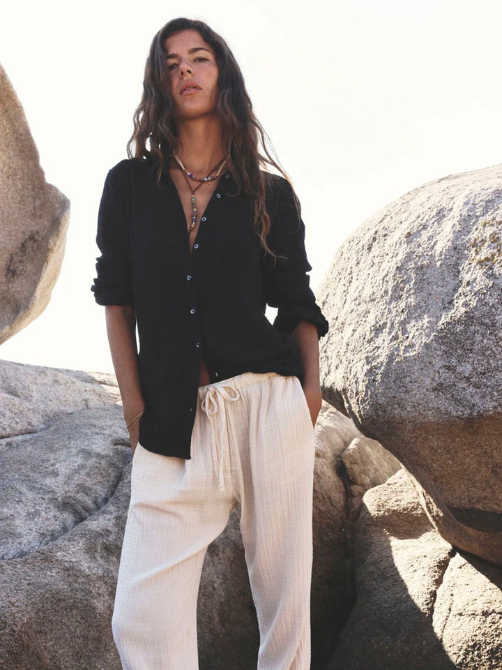 Woman standing on a rocky surface wearing a black shirt and white pants.