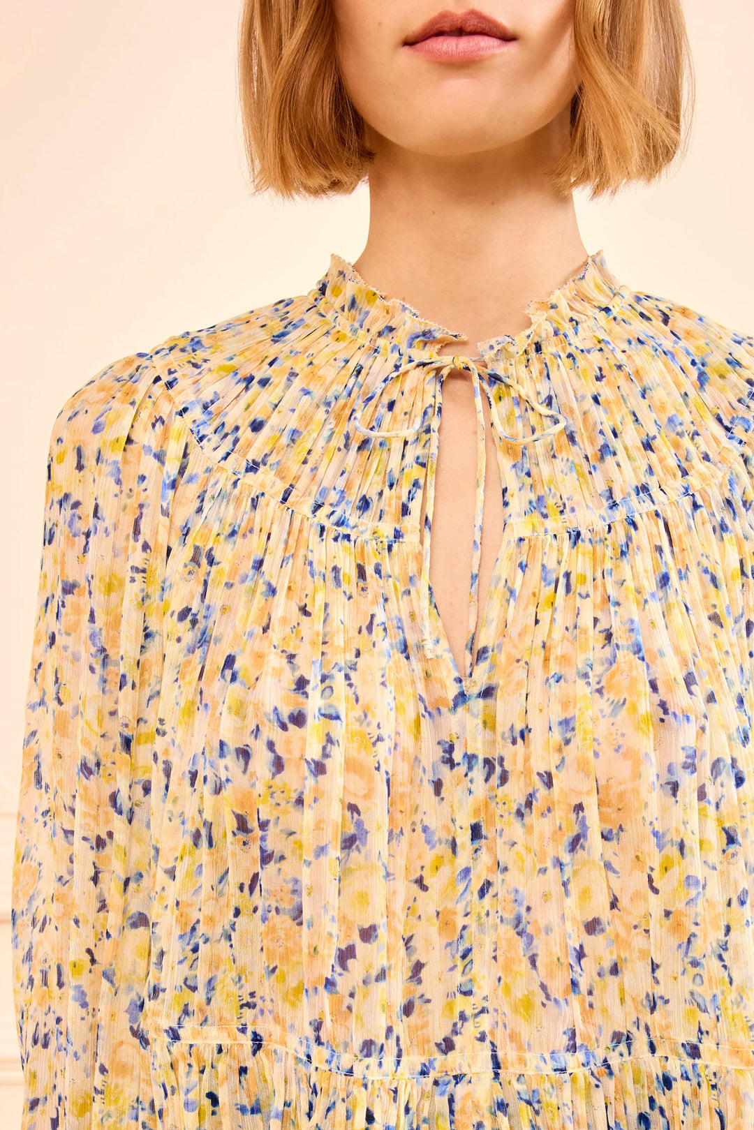 Yellow floral blouse worn by a person on a beige background