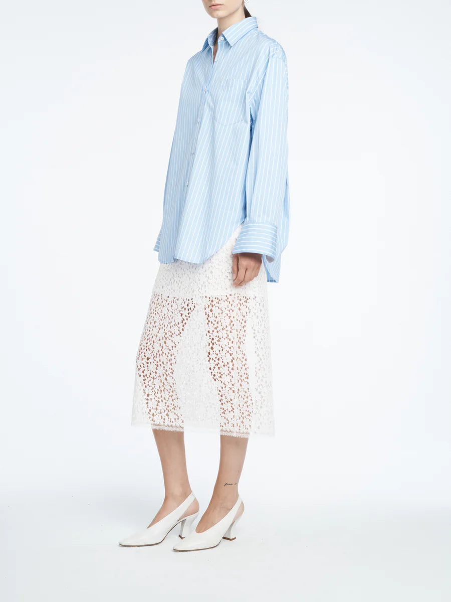 Person wearing a light blue striped shirt and white lace skirt on a white background
