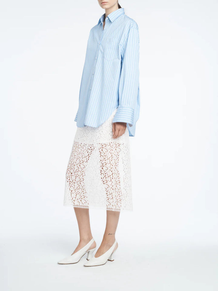 Person wearing a light blue striped shirt and white lace skirt on a white background