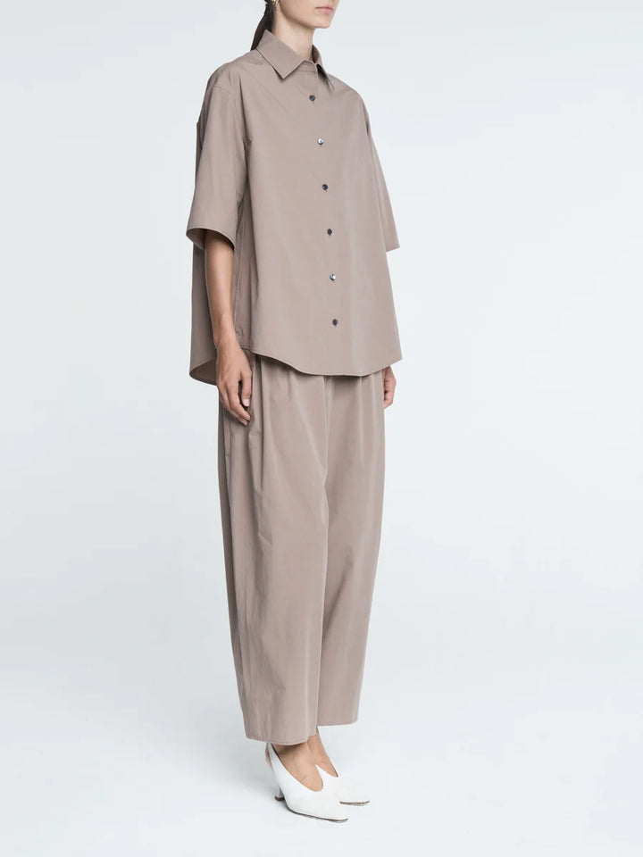 Person wearing a beige shirt and pants on a white background