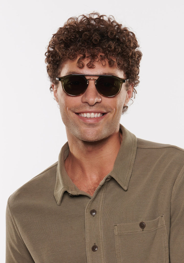 Man wearing sunglasses and a green shirt against a white background