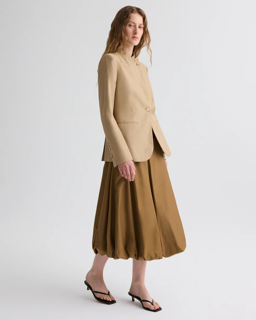 Woman wearing a beige blazer and brown skirt on a white background