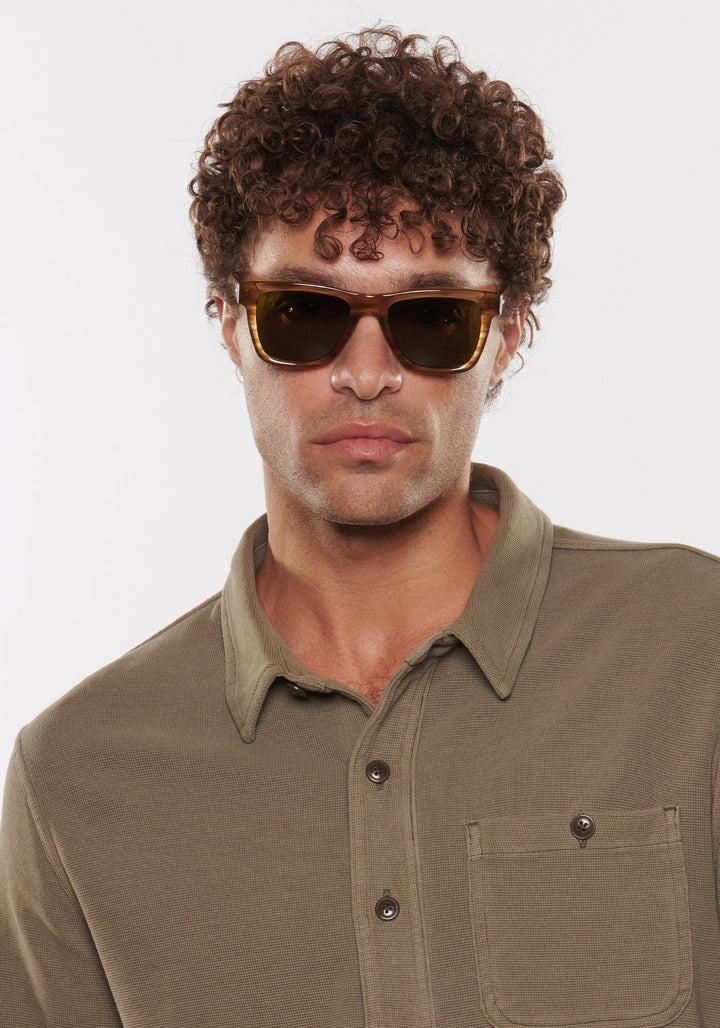 Man wearing sunglasses and a green shirt against a white background