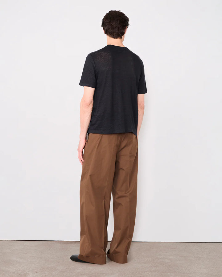 Person wearing a black t-shirt and brown pants standing against a white wall.