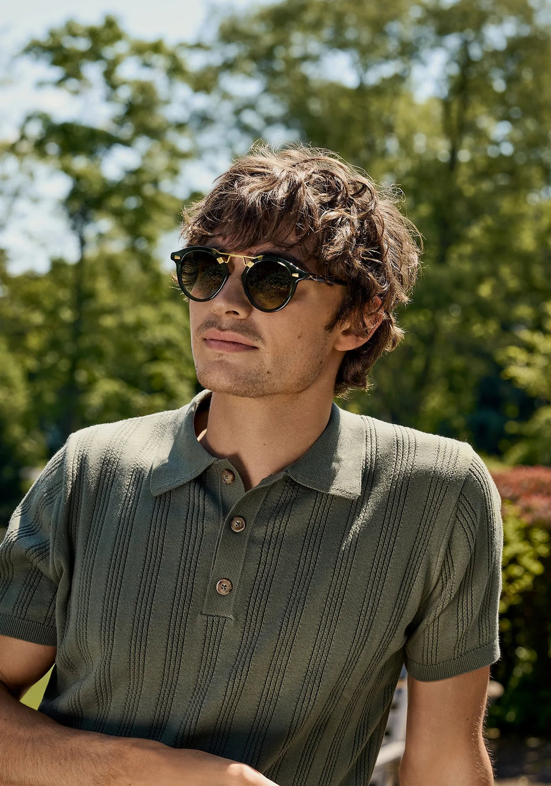 Man wearing sunglasses and a green polo shirt in a park setting