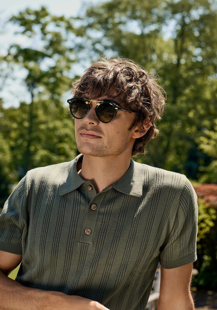 Man wearing sunglasses and a green polo shirt in a park setting