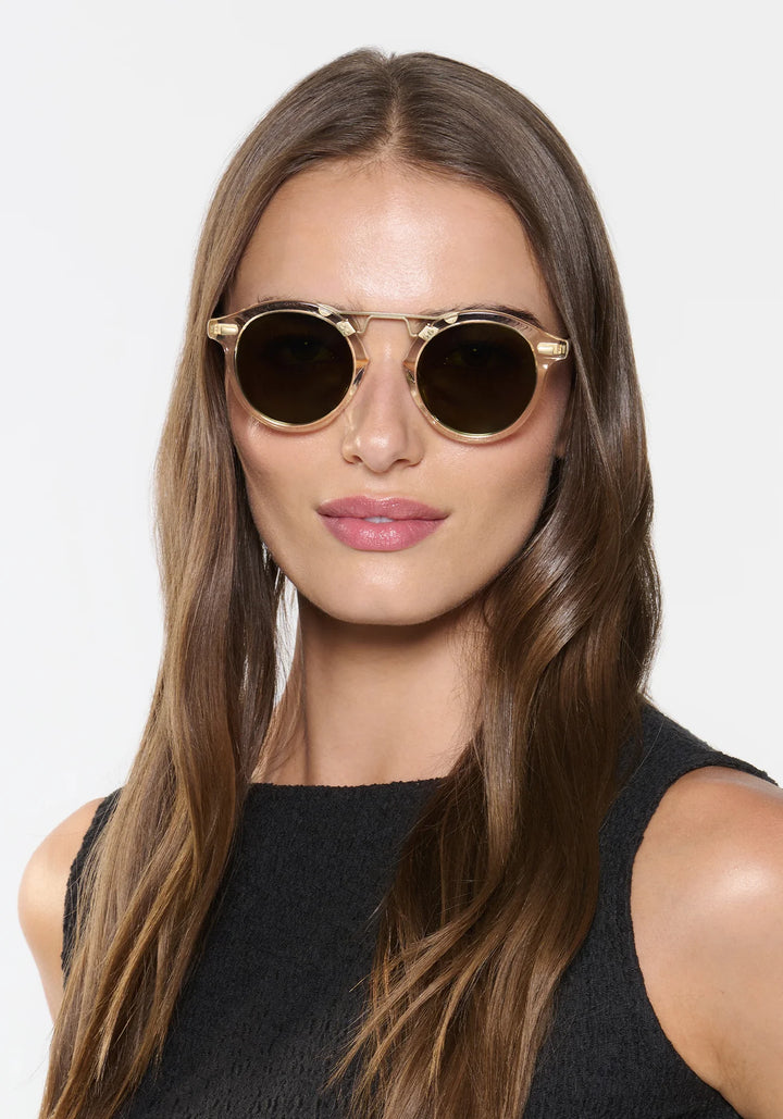 Woman wearing gold-framed sunglasses with a plain background