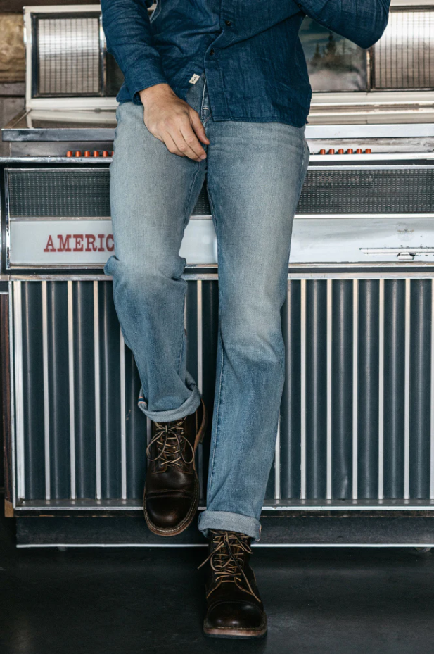 Person wearing blue jeans and brown boots standing in front of a vintage jukebox.