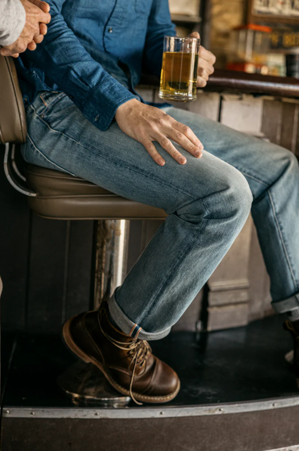 Person sitting on a bar stool holding a glass of beer in a casual setting.