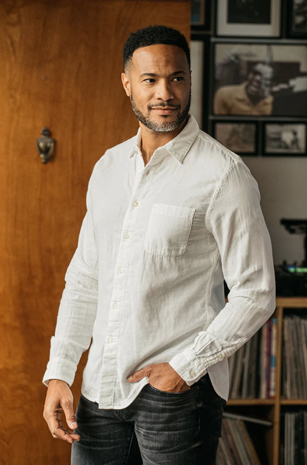Man wearing a white shirt standing in a room with wooden walls and bookshelves.