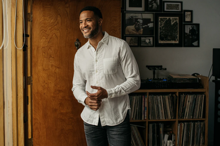 Man in a white shirt standing in a room with wooden paneling and vinyl records.