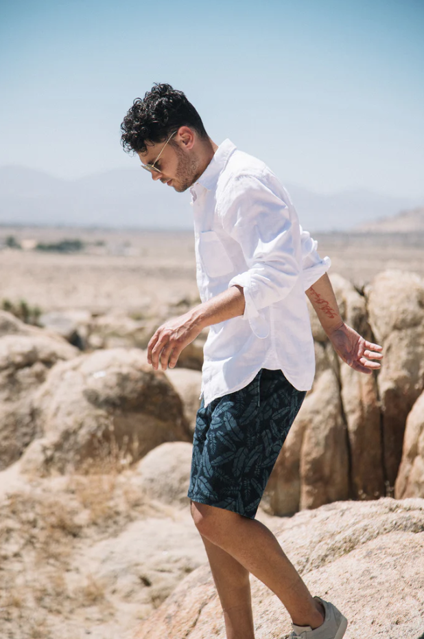 Man in white shirt and dark shorts standing on rocky terrain with clear sky