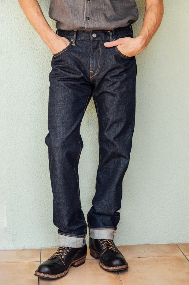 Person wearing dark blue jeans and black shoes against a light background