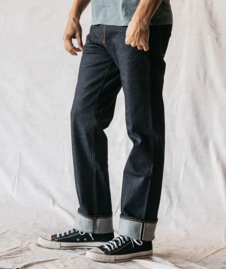 Person wearing dark jeans and black sneakers on a plain background
