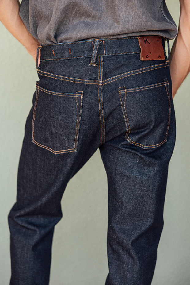 Person wearing dark blue jeans with a visible brand patch on a plain background