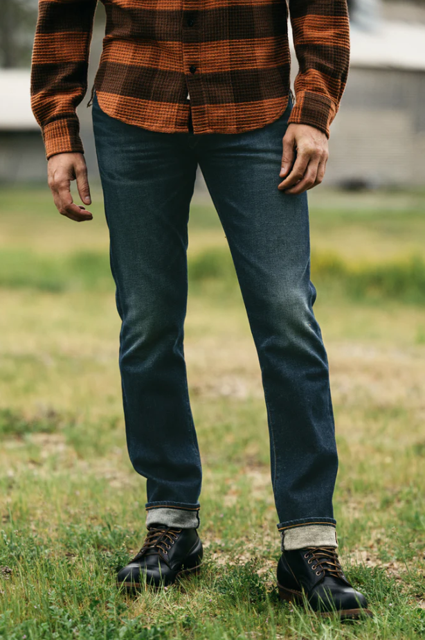 Person wearing a plaid shirt, jeans, and boots standing in a grassy area.