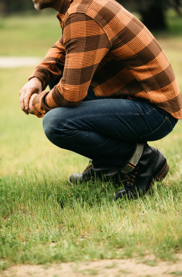 Person wearing a plaid shirt and jeans, crouching on grass