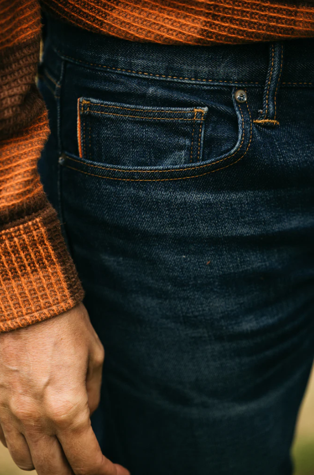 Close-up of dark blue jeans with a person wearing an orange sweater.