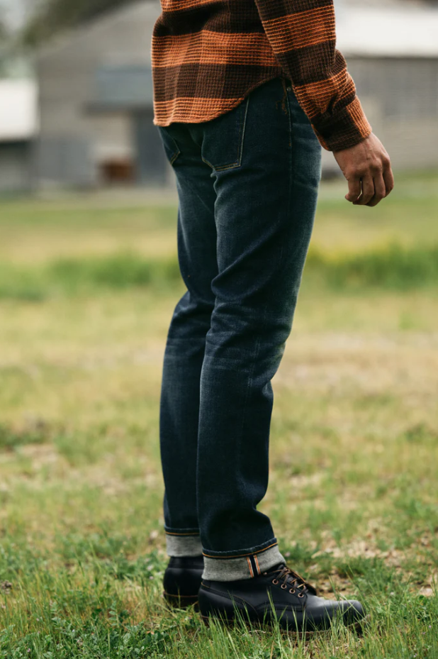 Person wearing a plaid shirt, jeans, and boots standing in a grassy area.