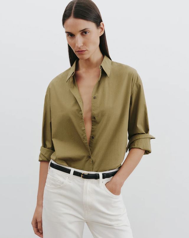 Woman wearing an olive green shirt and white pants on a plain background