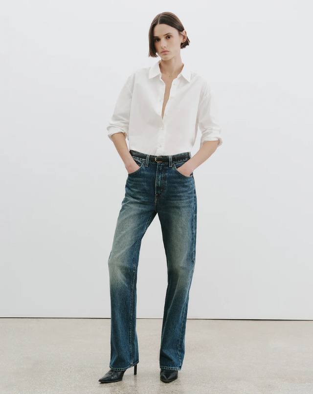 Woman wearing a white shirt and blue jeans against a plain background