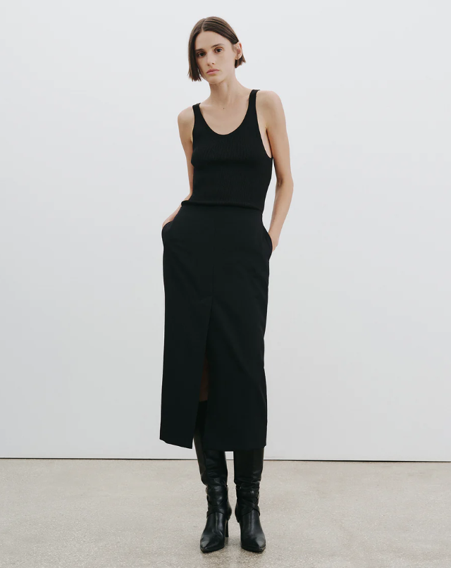 Person wearing a black sleeveless top and black skirt with black boots on a white background