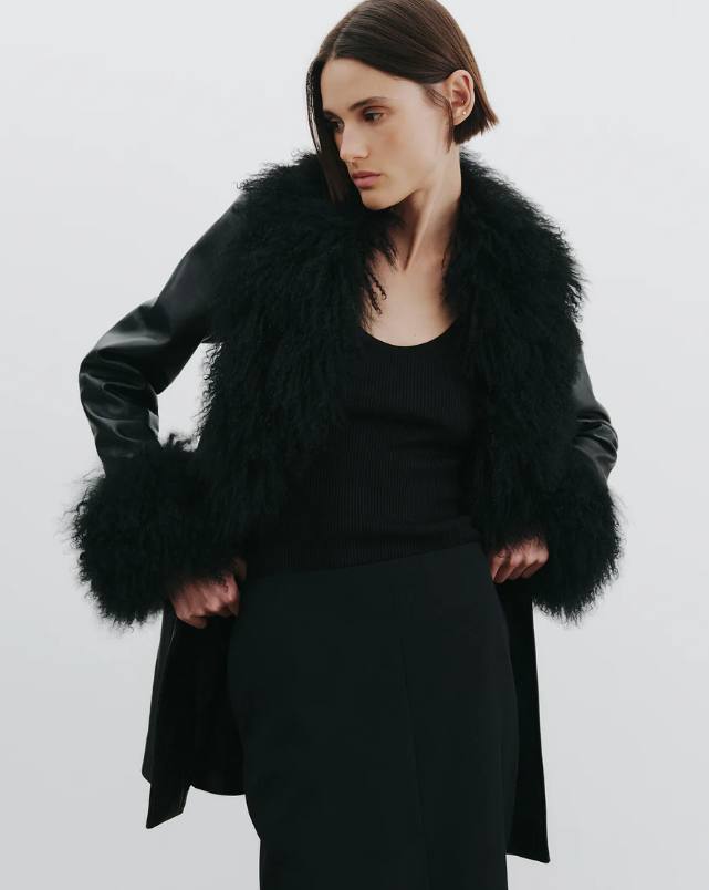 Woman wearing a black coat with a fur collar on a plain background