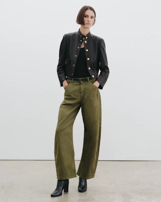 Person wearing a black jacket, black shirt, and green pants against a white background