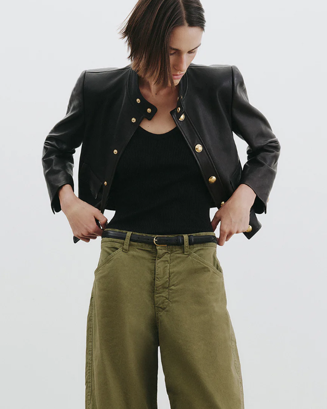 Person wearing a black jacket with gold buttons, black top, and green pants on a white background