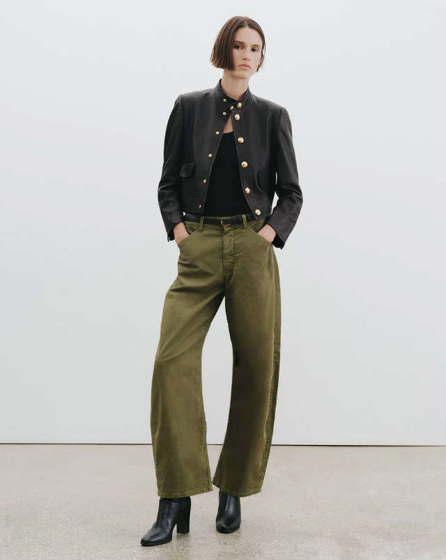 Person wearing a black jacket, black shirt, and green pants against a white background