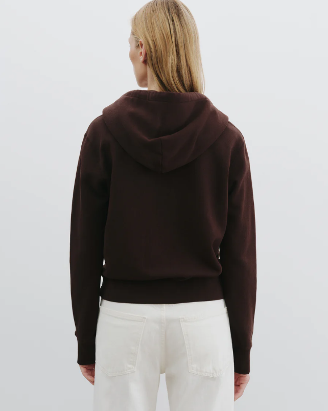 Person wearing a brown hoodie and white pants on a light gray background