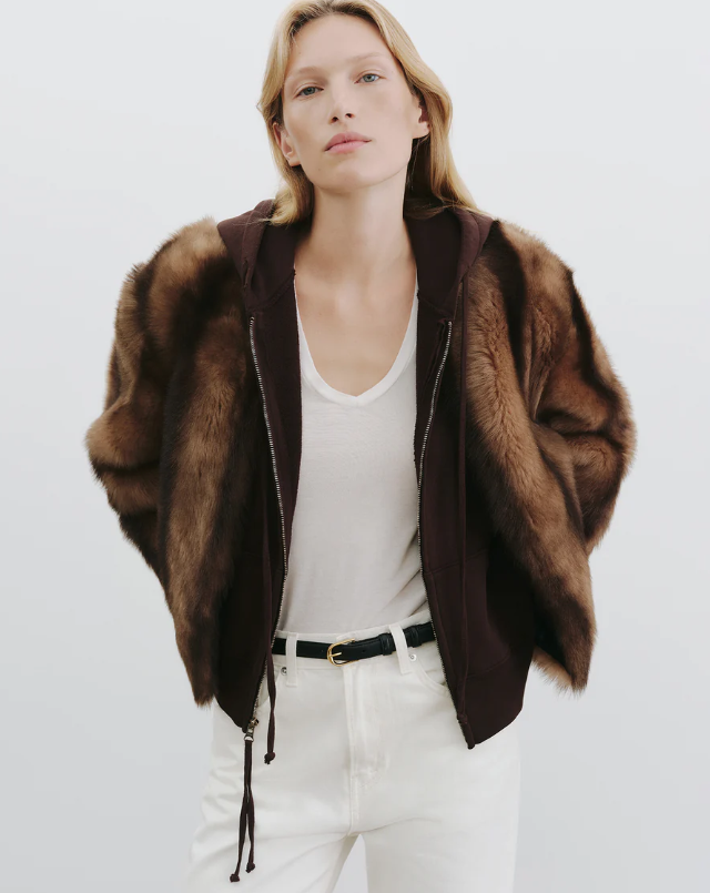 Person wearing a brown fur coat over a white outfit on a plain background