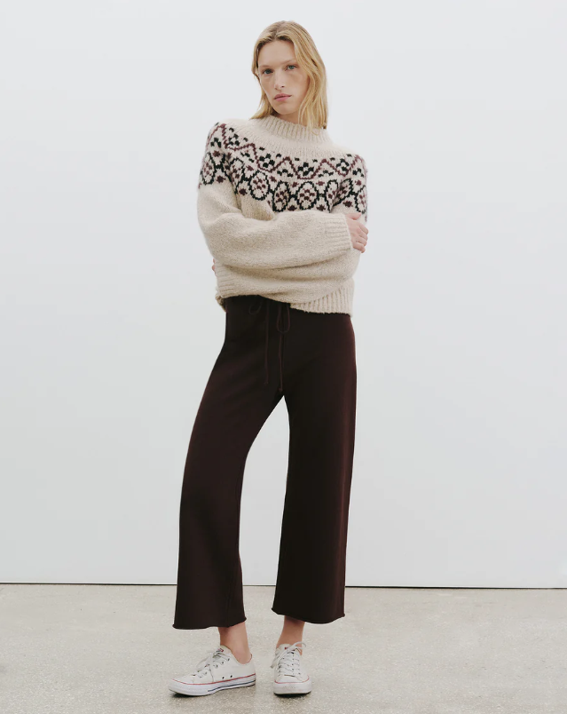 Person wearing a patterned sweater and dark pants against a white background