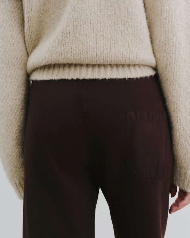 Brown pants with a brand logo worn by a person wearing a beige sweater on a light gray background