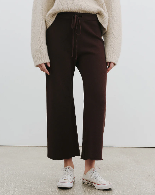 Person wearing brown pants and a beige sweater against a white background