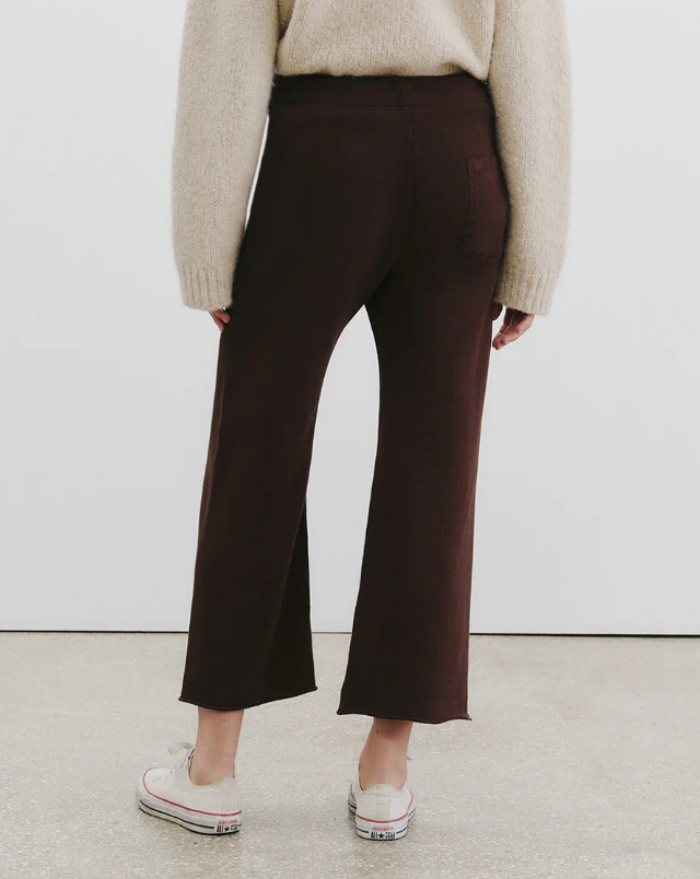 Person wearing brown pants and a beige sweater against a white background