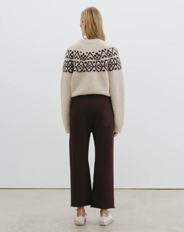 Person wearing a patterned sweater and dark pants against a white background