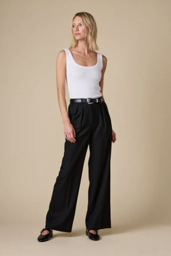 Woman wearing a white tank top and black wide-leg pants on a beige background