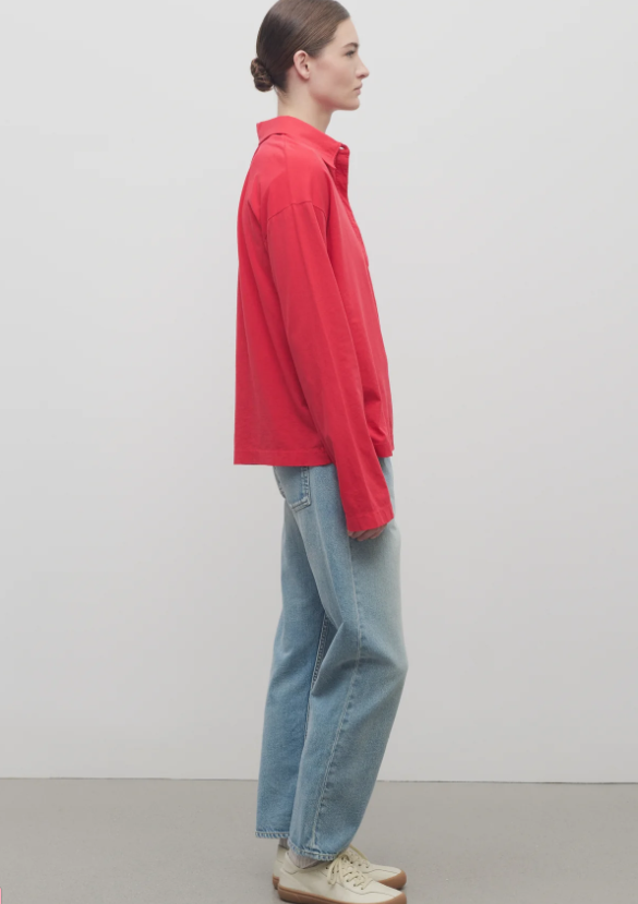 Person wearing a red shirt and blue jeans standing against a plain background.