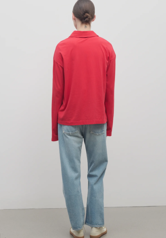 Person wearing a red sweater and light blue jeans against a plain background.