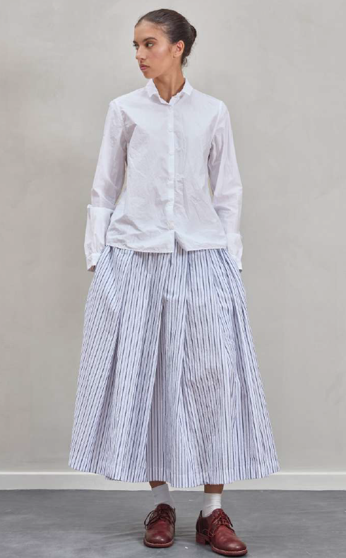 Woman wearing a white shirt and striped skirt against a plain background