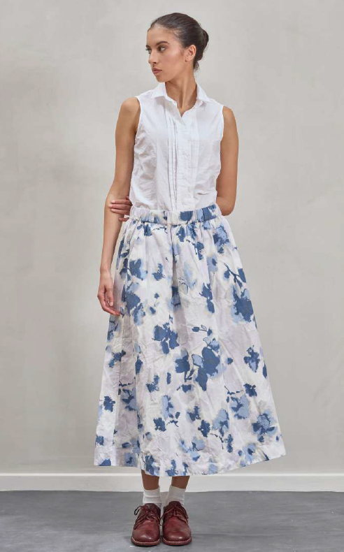Woman wearing a white sleeveless top and floral skirt against a plain background