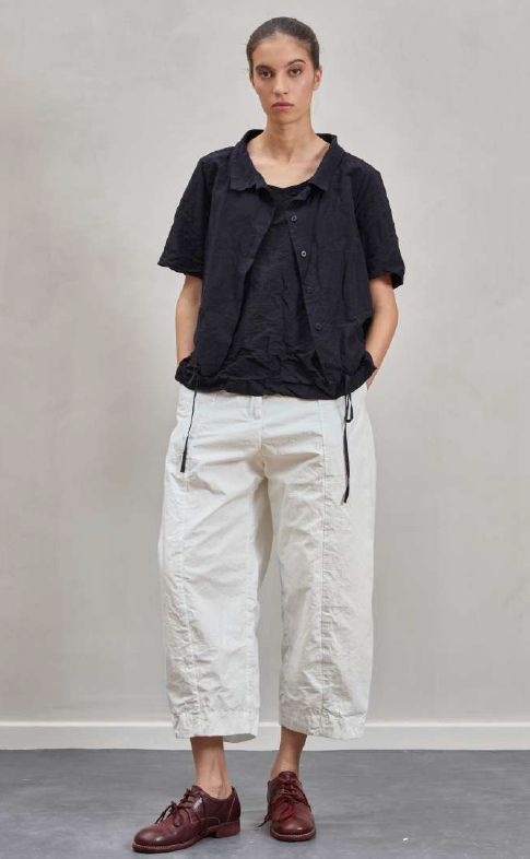 Person wearing a black shirt and white pants against a plain background