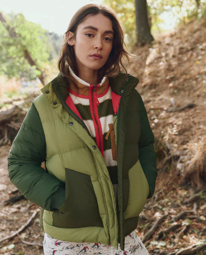 Woman wearing a green puffer vest over a colorful hoodie in a forest setting