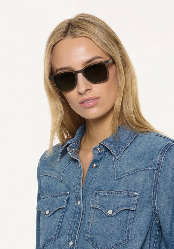 Woman wearing black sunglasses and a denim shirt on a white background