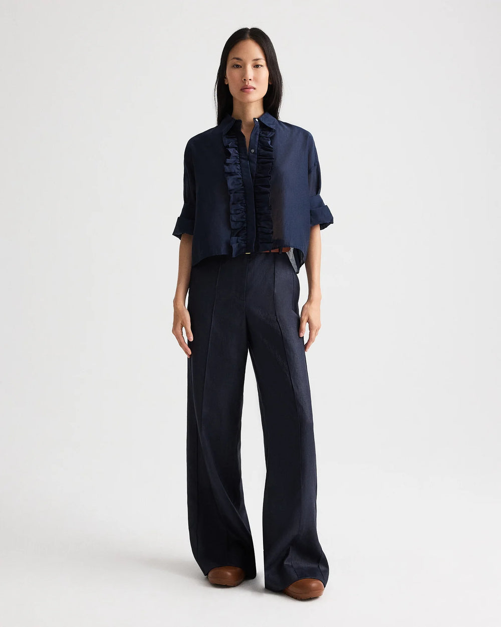 Woman wearing a navy blue blouse and wide-leg pants on a white background