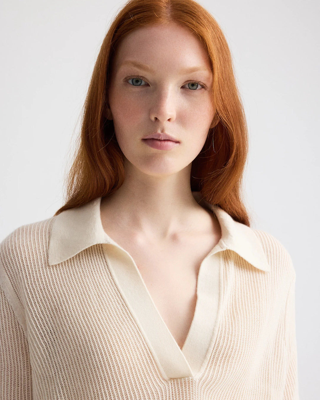 Woman wearing a beige sweater with a white collar against a plain background